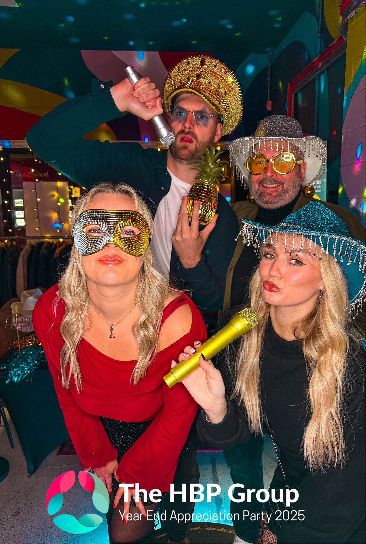 Four colleagues in masks and glitter hats posing at The HBP Group year end party, with their logo on the print