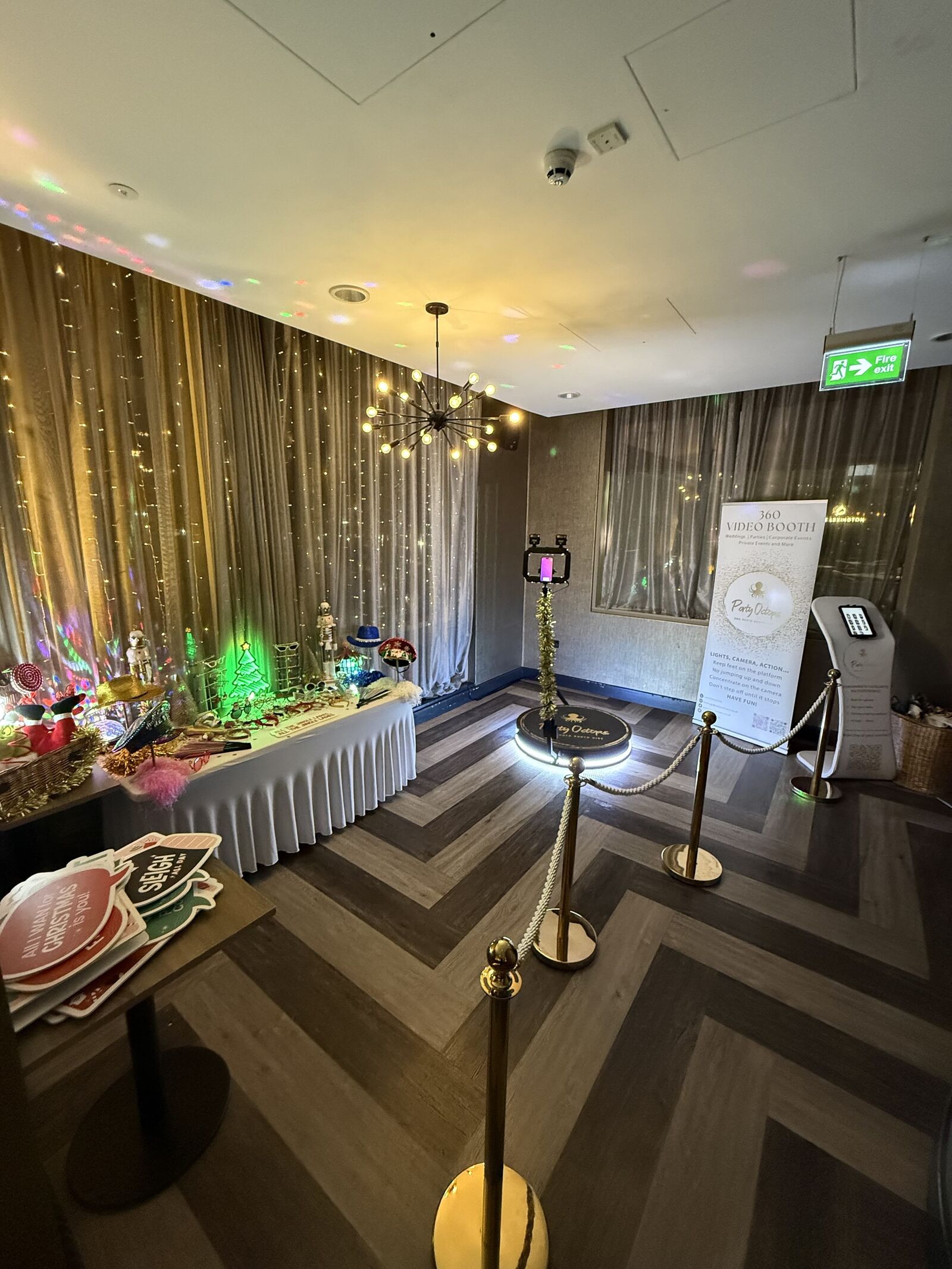 The Party Octopus 360 booth set up at a hotel Christmas party — lit platform, gold rope barrier, styled prop table and sharing station